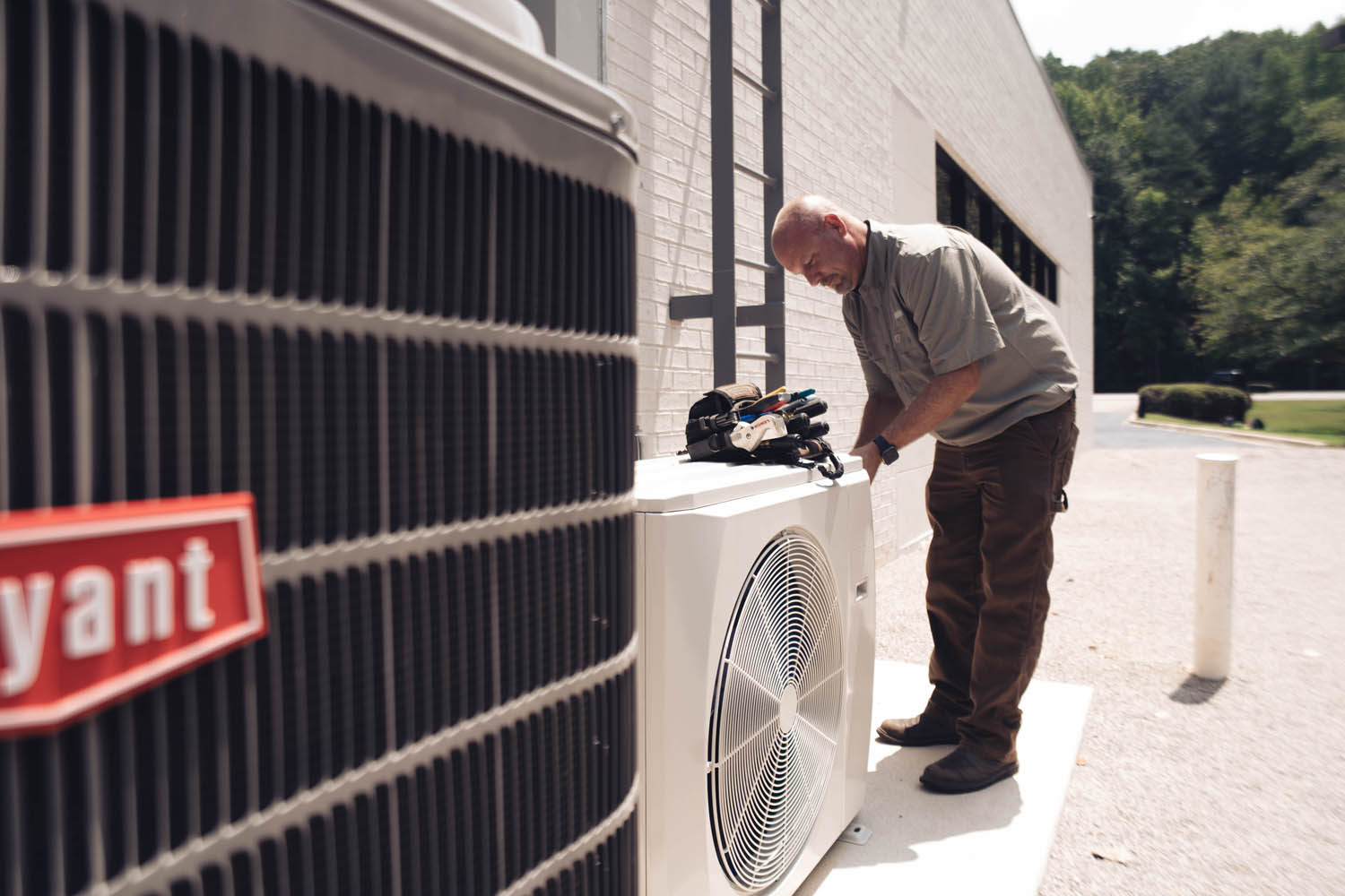 Technician repairing outdoor AC unit next to Bryant HVAC system.
