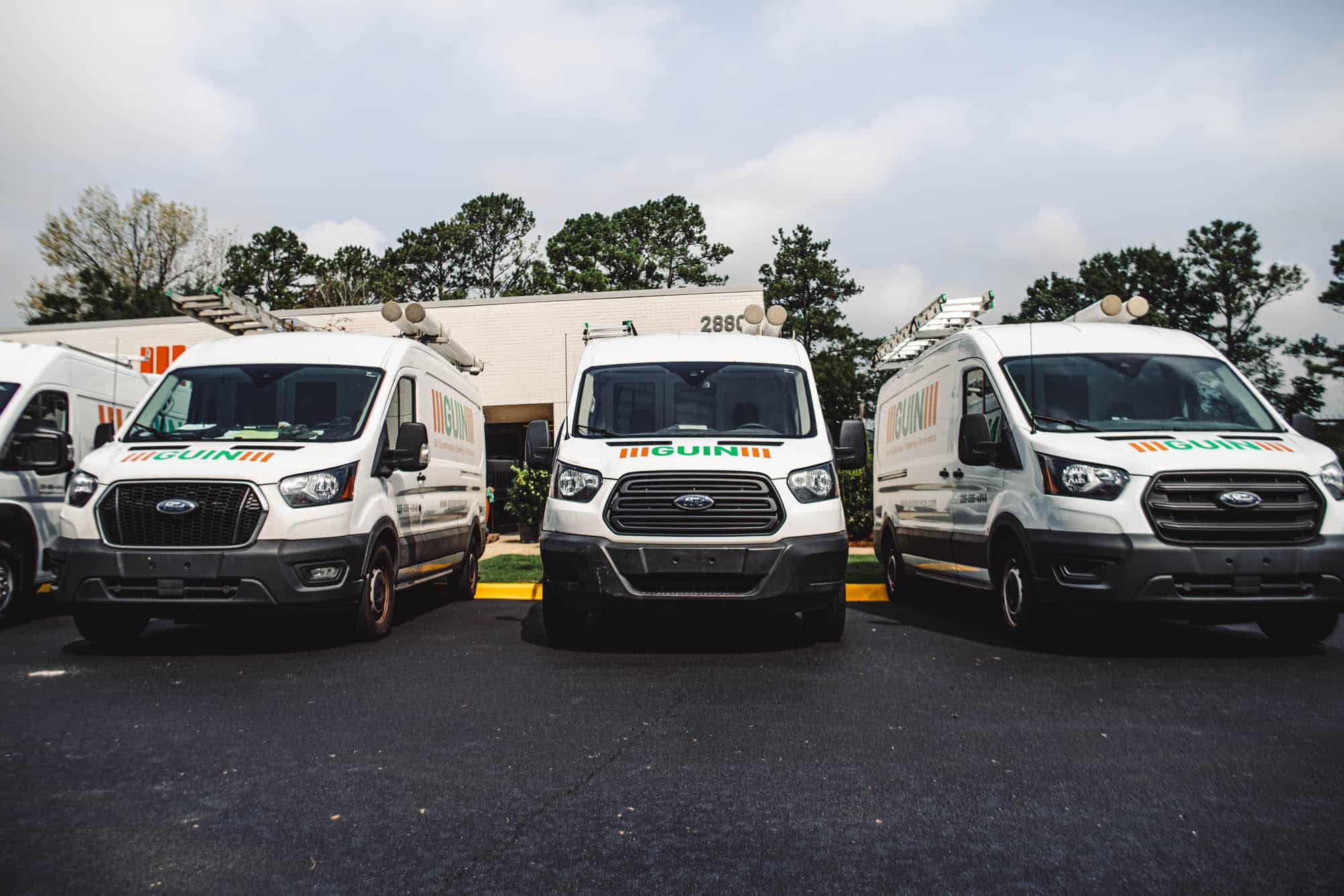 Three Guin service vans parked outside a building with trees in the background.